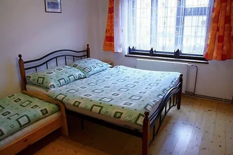 Pokoj s kovovou manželskou postelí a lůžkem u okna