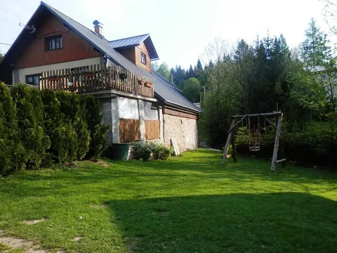 Travnatá zahrada s houpačkou, v pozadí chalupa s balkonem a les